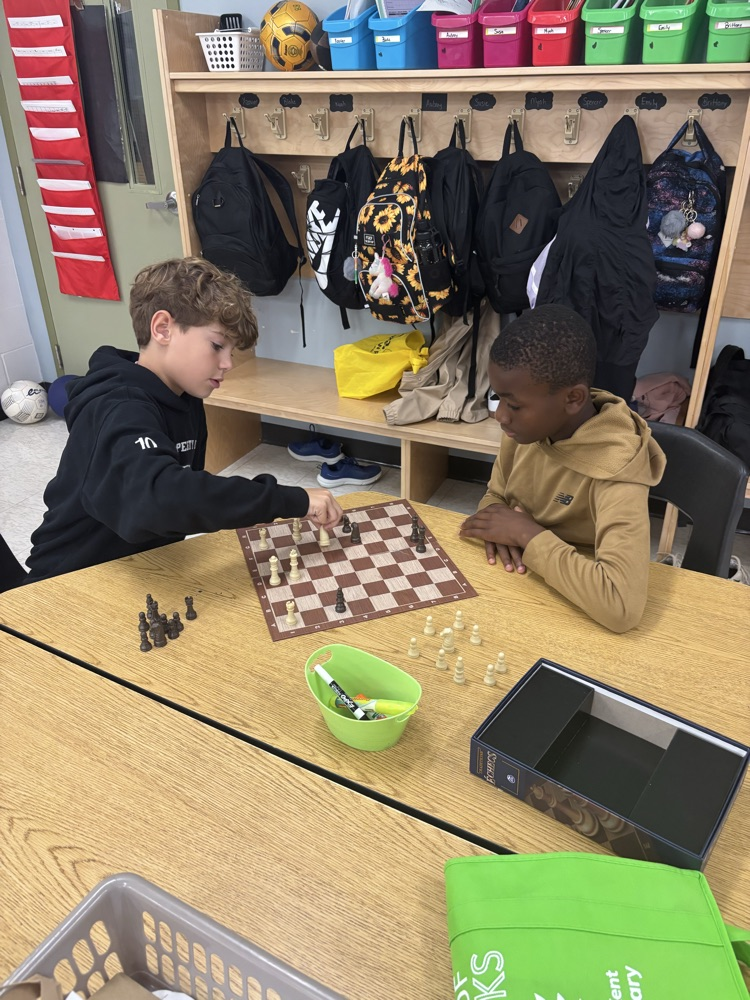 two grade 5 boys siting at a table in a classroom playing chess