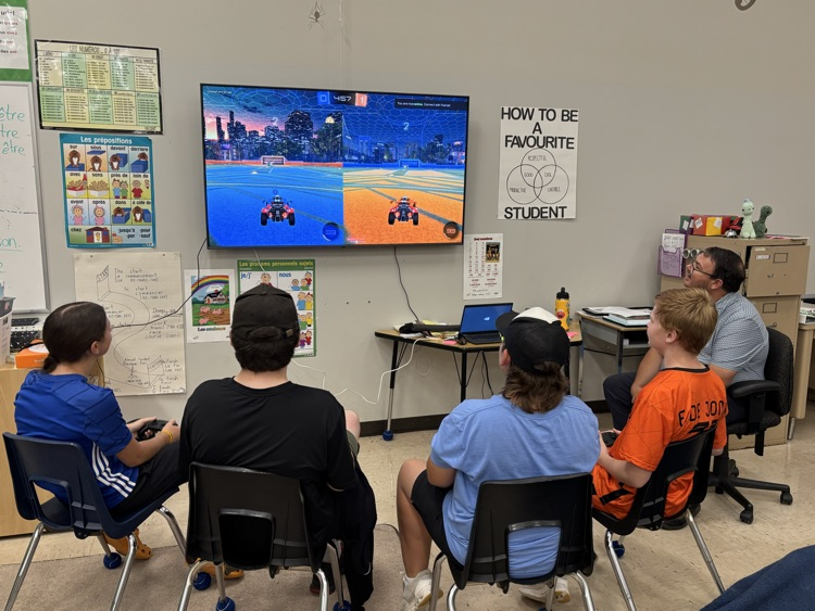one male teacher and 4 grade 8 students sitting in chairs playing Esports