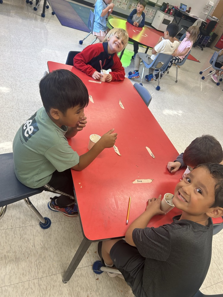 students sitting a red table eating applesauce
