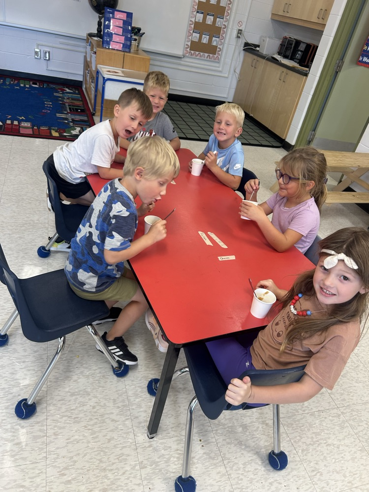 students sitting a red table eating applesauce