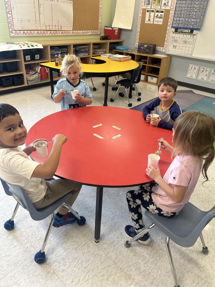 students sitting a red table eating applesauce