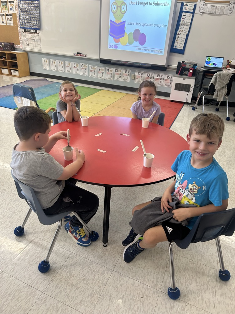 students sitting a red table eating applesauce