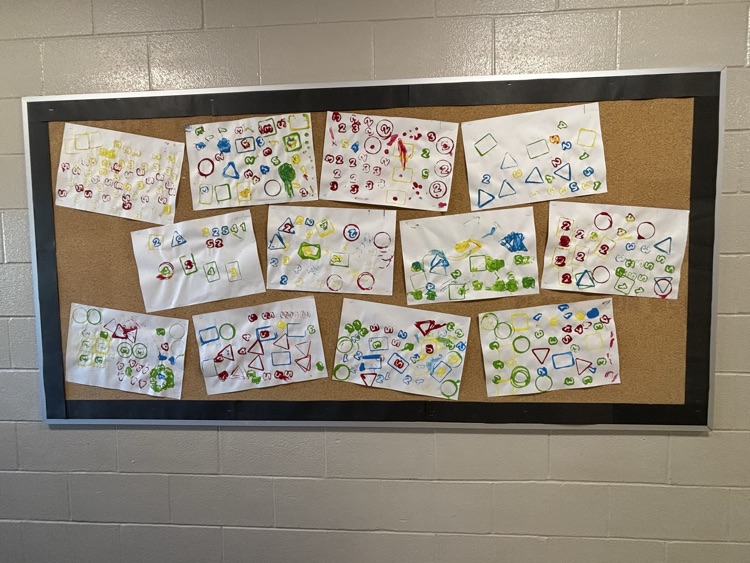 A school bulletin board with kindergarten math/artwork. Mixing colors, shapes, and numbers using stamps and paint.