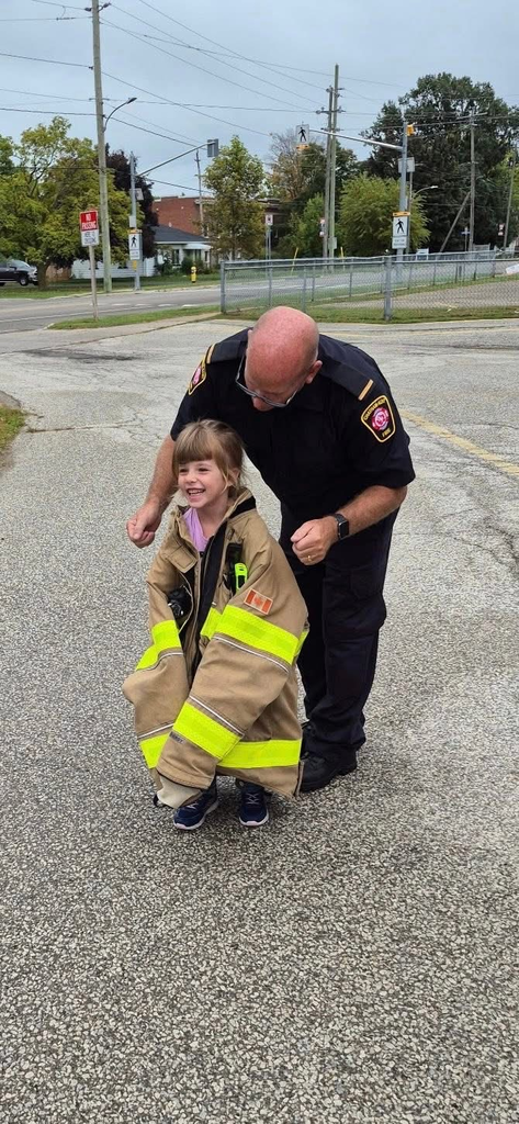 A Wheatley firefighter, letting a young female student try on the fire coat