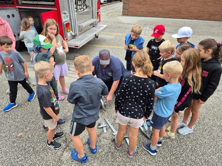 A group of students listening to the firefighter out by the fire truck