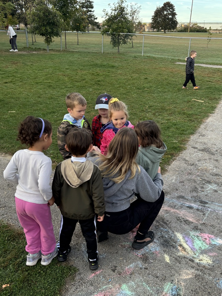 A grade 7 female student crouched down, talking to a group of kindergarten students