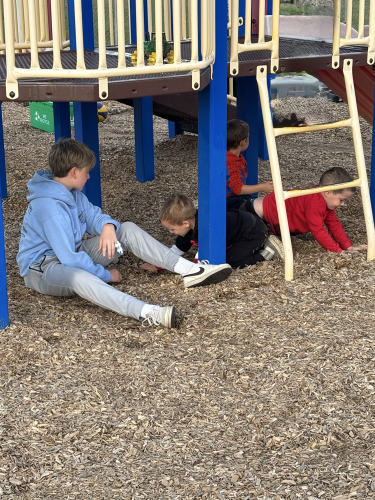 A grade 7 student sitting underneath the kindergarten climber playing with kindergarten students