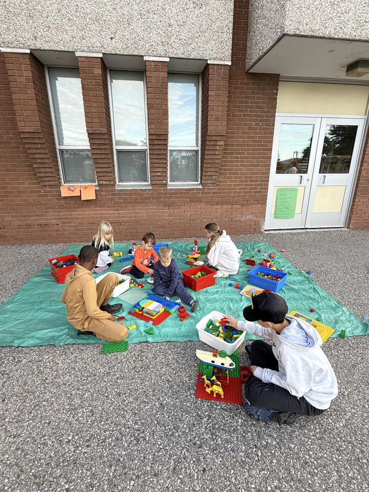 Group of students with older students playing Lego on a tarp outside