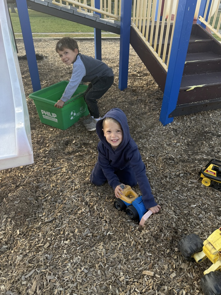 Two kindergarten children playing with trucks in the mulch