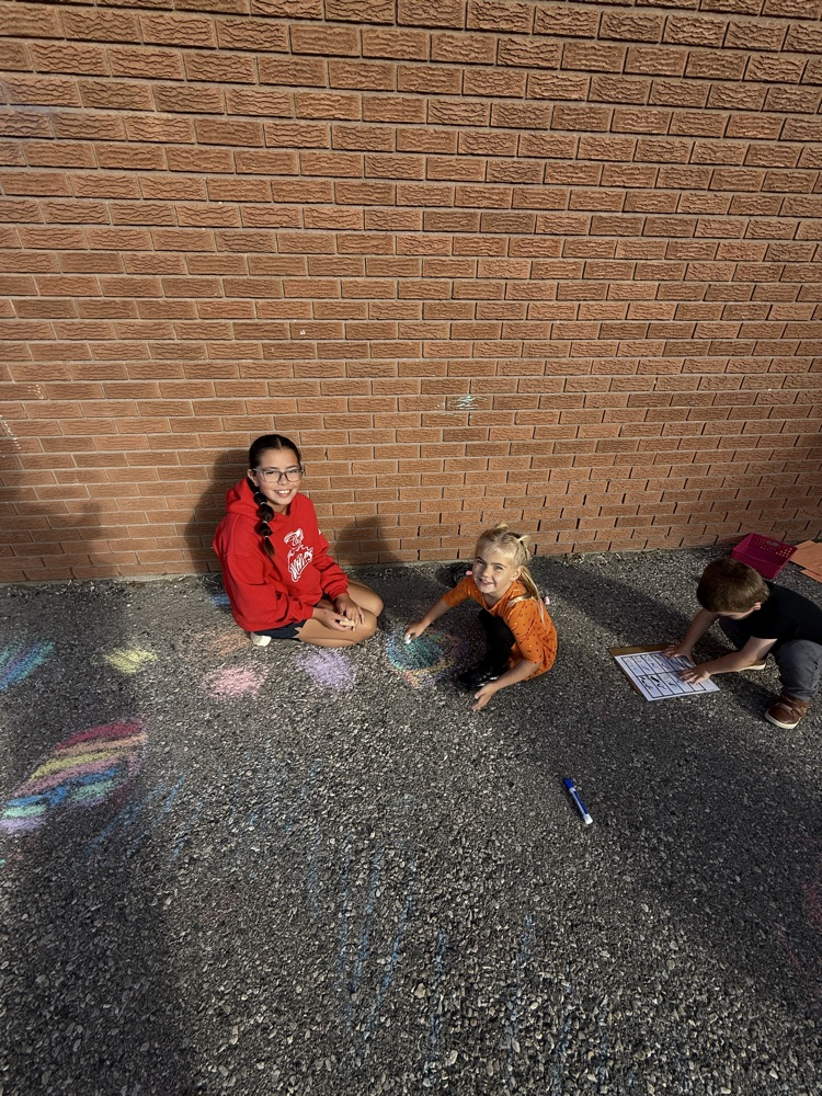 A couple of students creating art on the pavement with sidewalk chalk