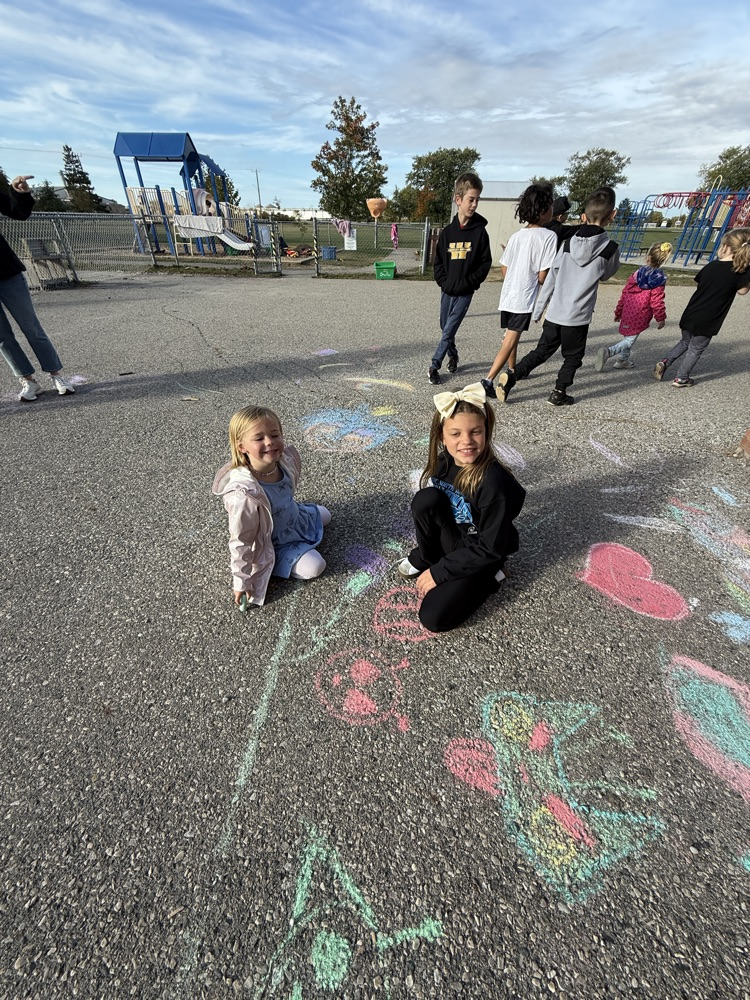 Two student students creating art with sidewalk chalk on the pavement at school