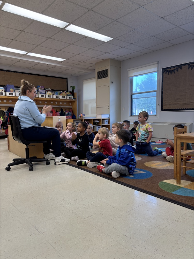 teacher sitting in chair working with students sitting on the floor in front of her