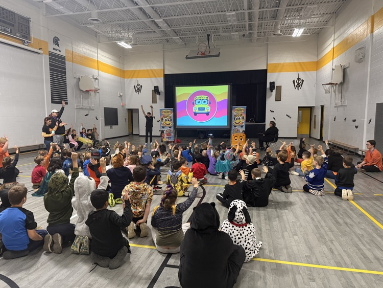 students in the gym sitting and listening to a bus safety presentation