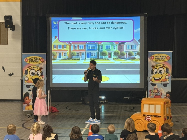 students in the gym sitting and listening to a bus safety presentation