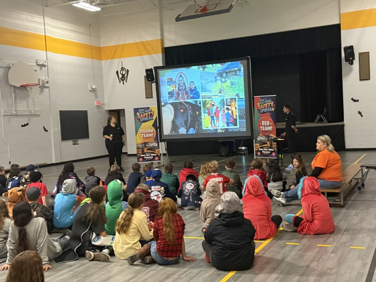 students in the gym sitting and listening to a bus safety presentation