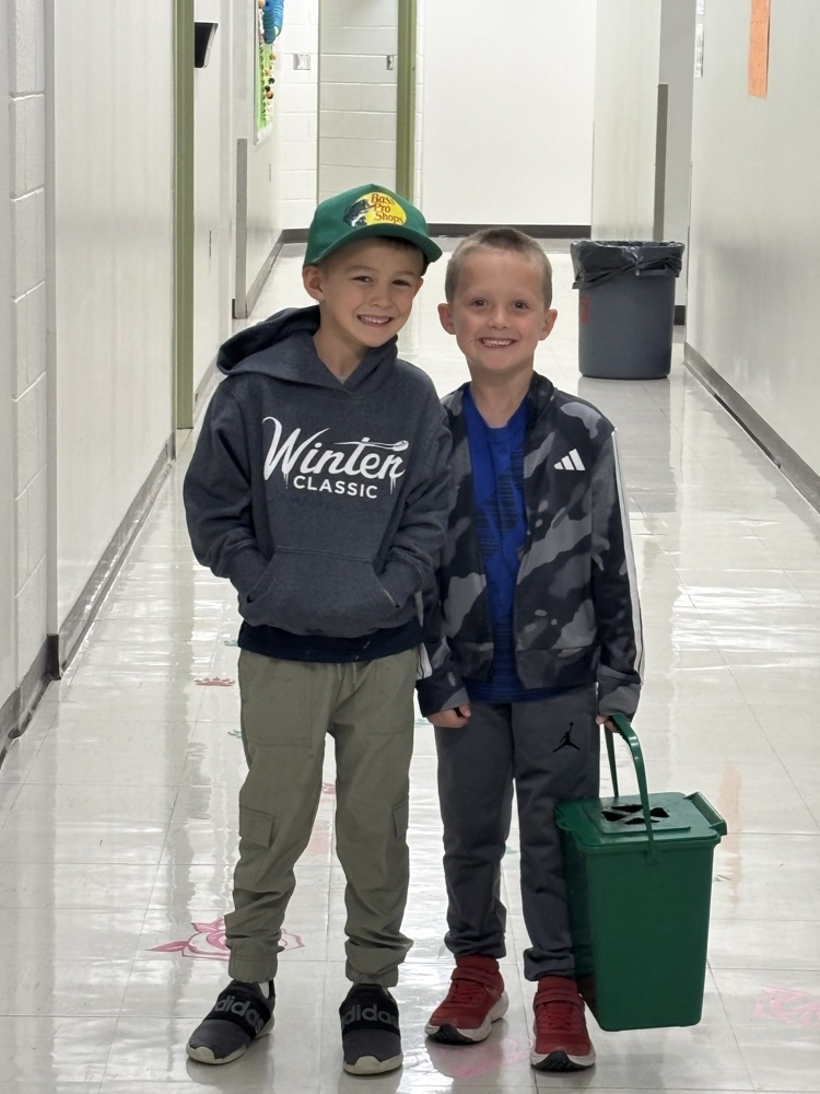 two boys smiling at the camera with a composting container