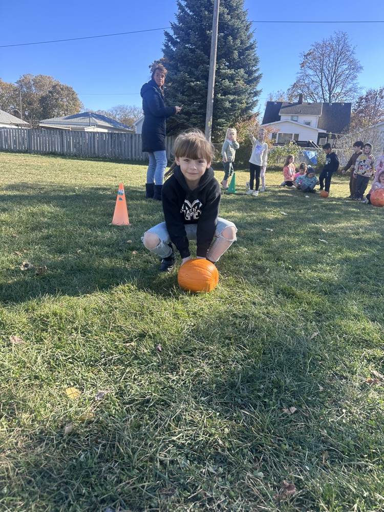 students rolling pumpkins across the grass