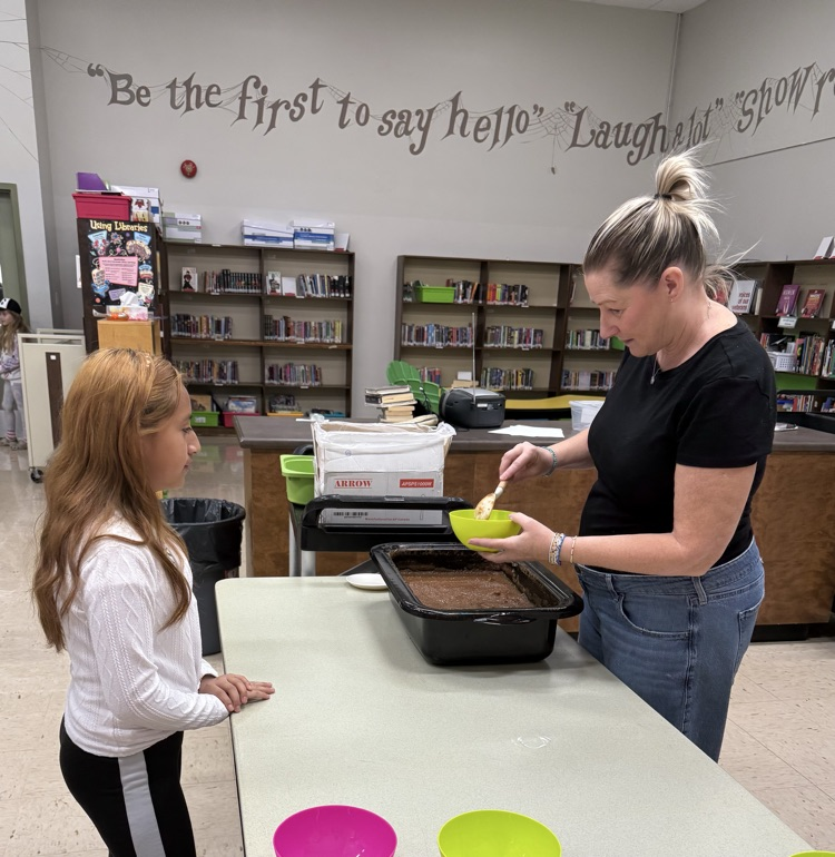 An adult serving applesauce to a student