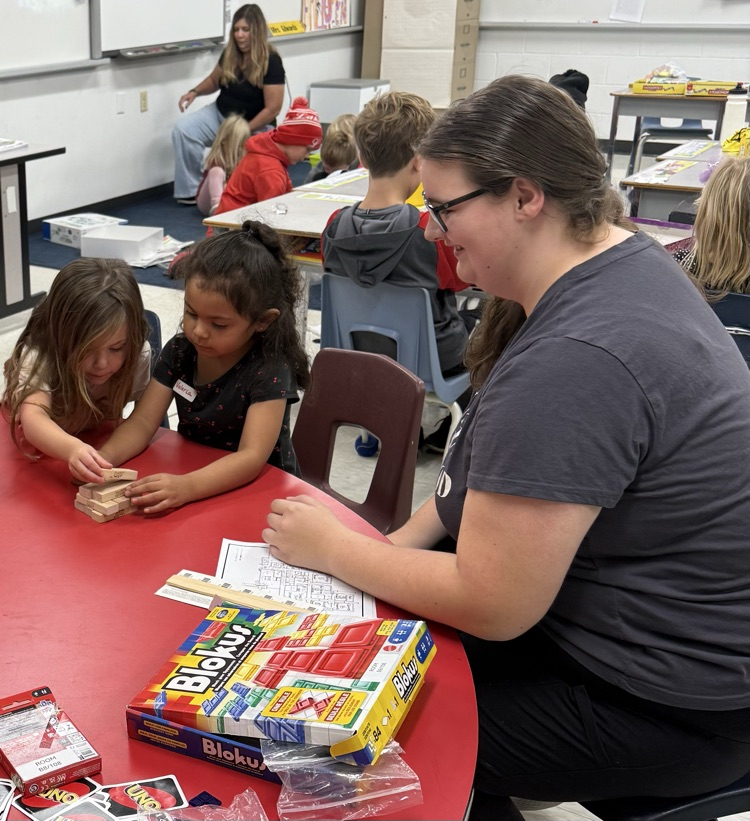 An older student volunteer watching two younger student students play Jenga