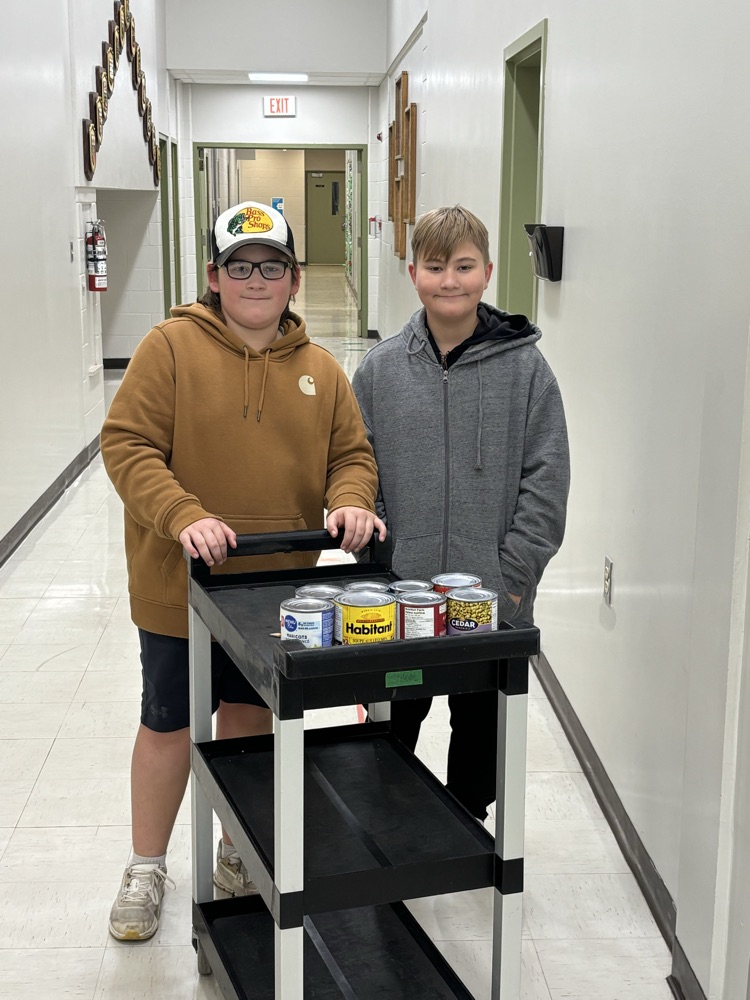 2 boys helping out with canned food drive. pushing a wheeled cart with canned goods.