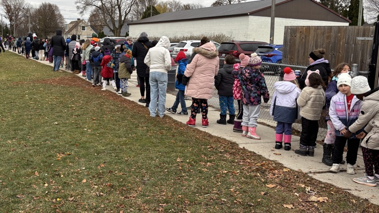 students standing in line on the sidewalk headed towards a field trip