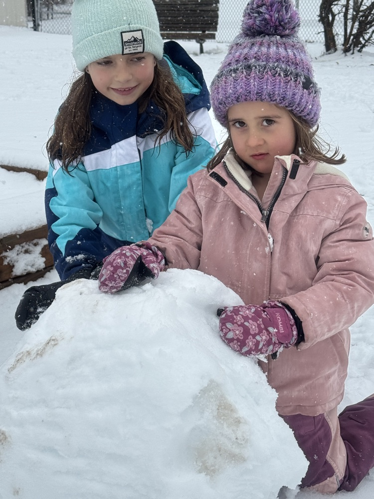 two people kneeling behind a snow ball