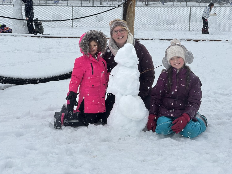 a couple of people kneeling beside a snowman 