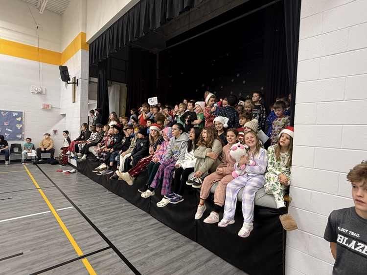 a large group of students sitting on the stage watching a volleyball game
