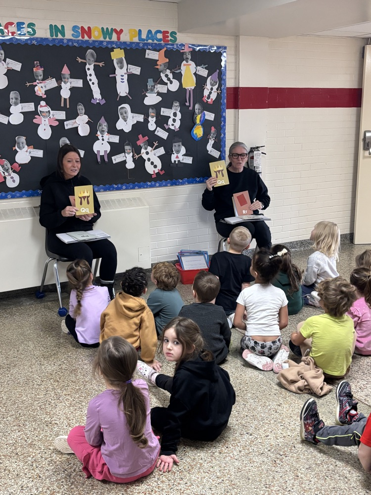 two teachers working with children sitting on the floor in front of them