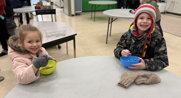 Two young students eating oatmeal at a table, smiling at the camera