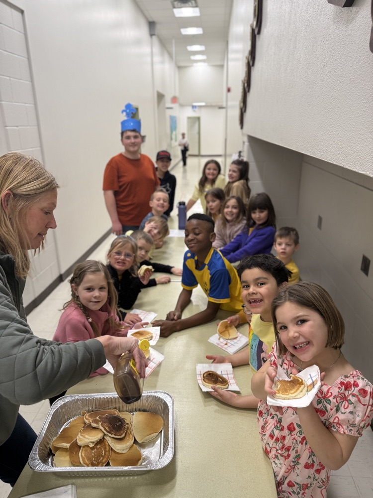 pancakes. a group of students standing at a table eating pancakes