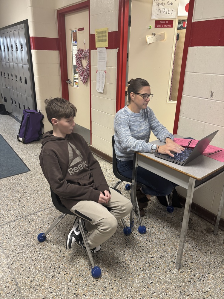 student sitting with teacher working on a laptop