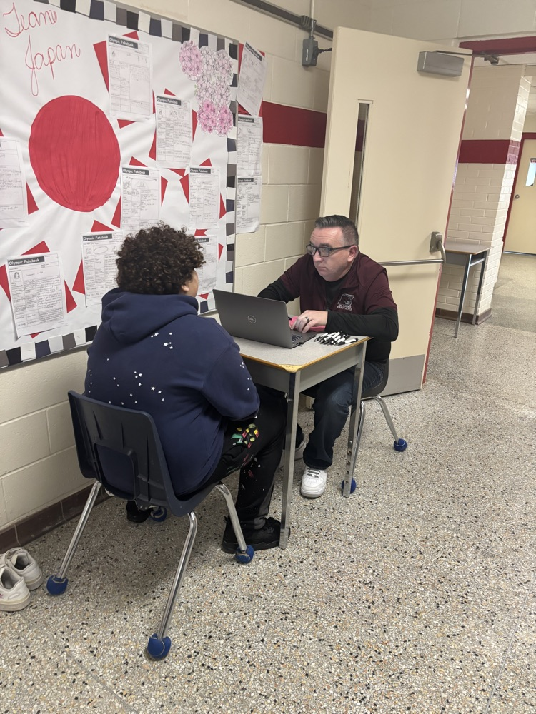Student sitting with teacher working on a laptop
