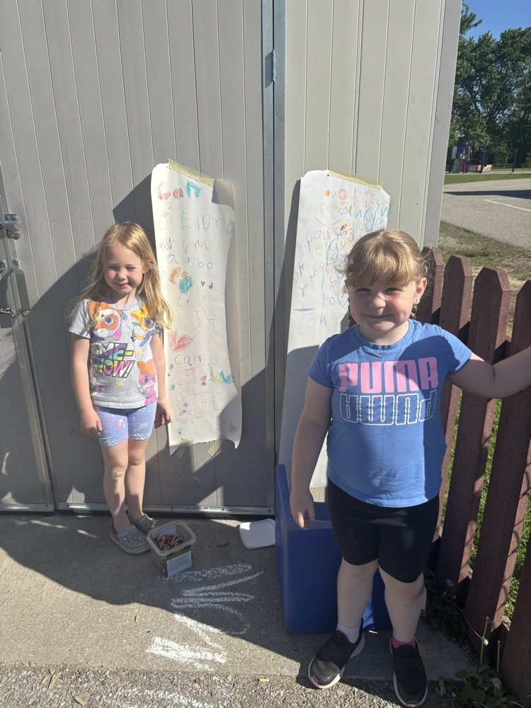 2 students standing beside their writing by the shed 