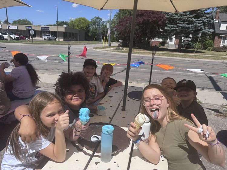 Children sitting at a picnic table, eating ice cream