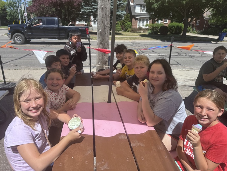 Children sitting at a picnic table, eating ice cream