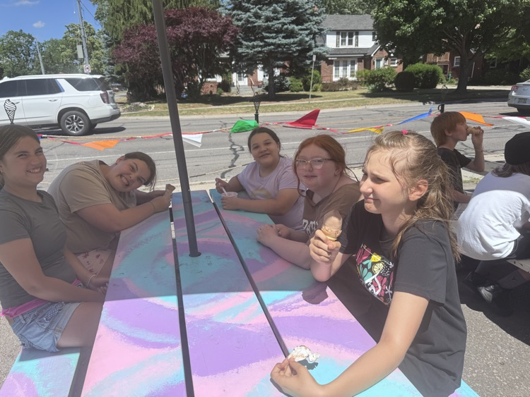 Children sitting at a picnic table, eating ice cream