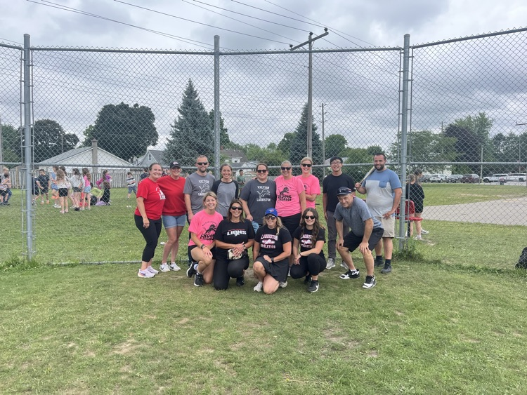 Group of staff members posing in front of baseball back
