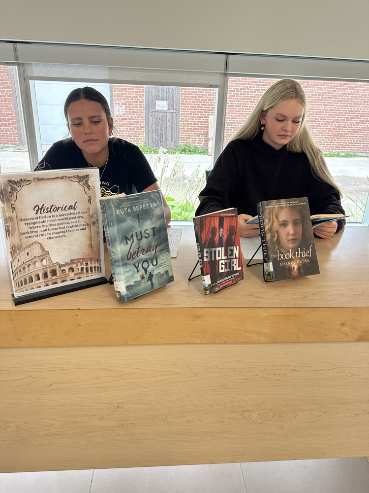 Grade 9 English students exploring books at different genre stations during a Book Tasting activity in the school library.