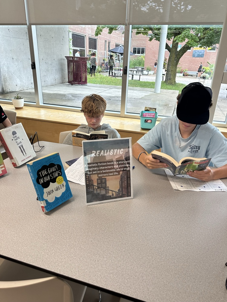Grade 9 English students exploring books at different genre stations during a Book Tasting activity in the school library.