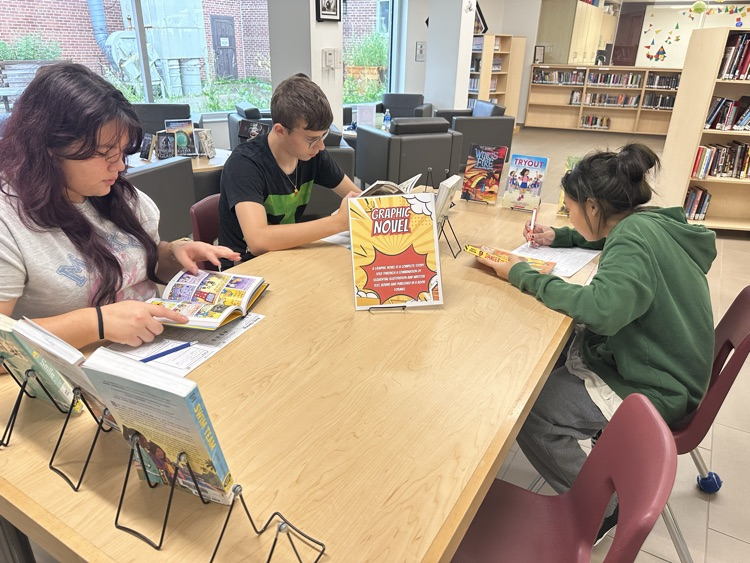 Grade 9 English students exploring books at different genre stations during a Book Tasting activity in the school library.