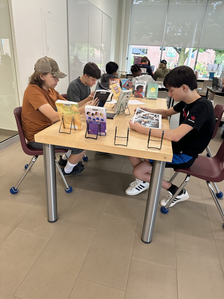 Grade 9 English students exploring books at different genre stations during a Book Tasting activity in the school library.