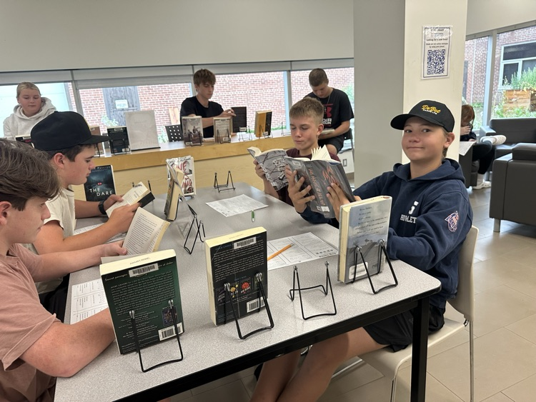 Grade 9 English students exploring books at different genre stations during a Book Tasting activity in the school library.