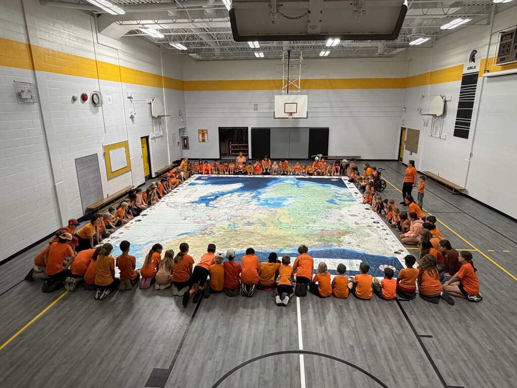 Students kneeling in orange shirts around a map of Canada