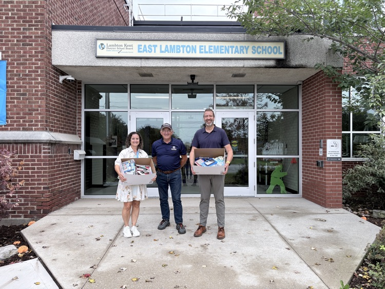 three adults, two holding boxes full of donated school supplies from Staples and Lambton Golden Kiwanis