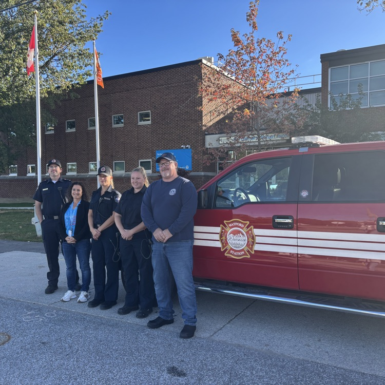 4 firefighters and the principal standing in front of the school by the fire department van