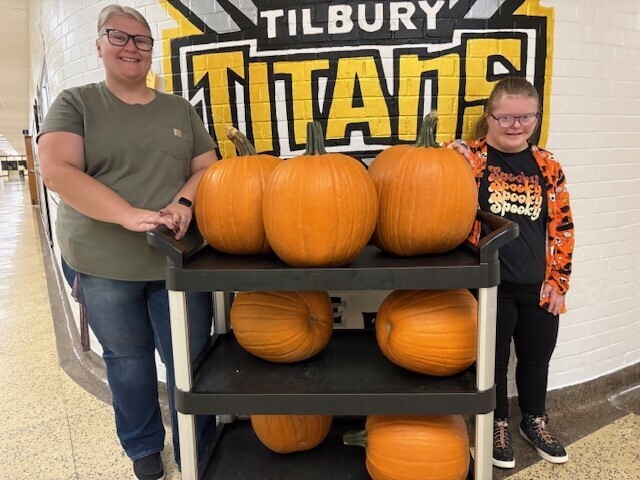 two people standing on either side of a cart full of pumpkins