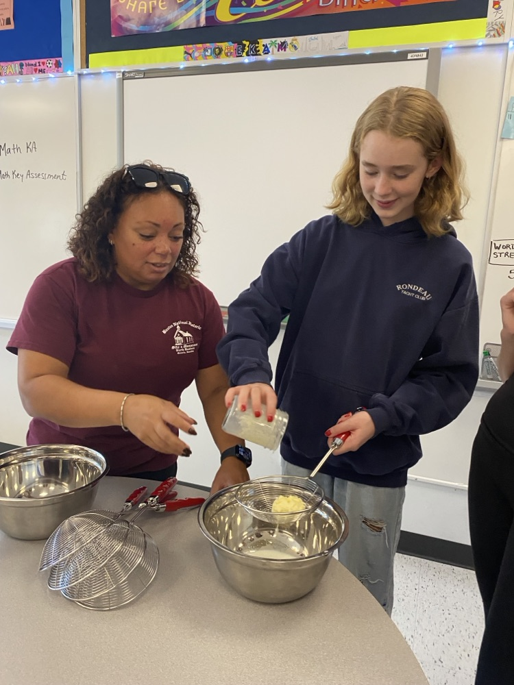 Woman and teenage student adding ingredients to a bowl to make butter.