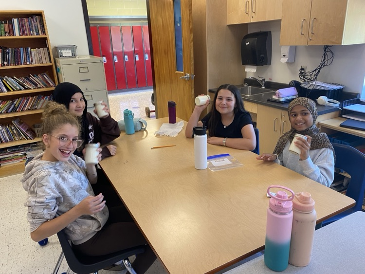 Students sitting at a table holding jars with butter ingredients.