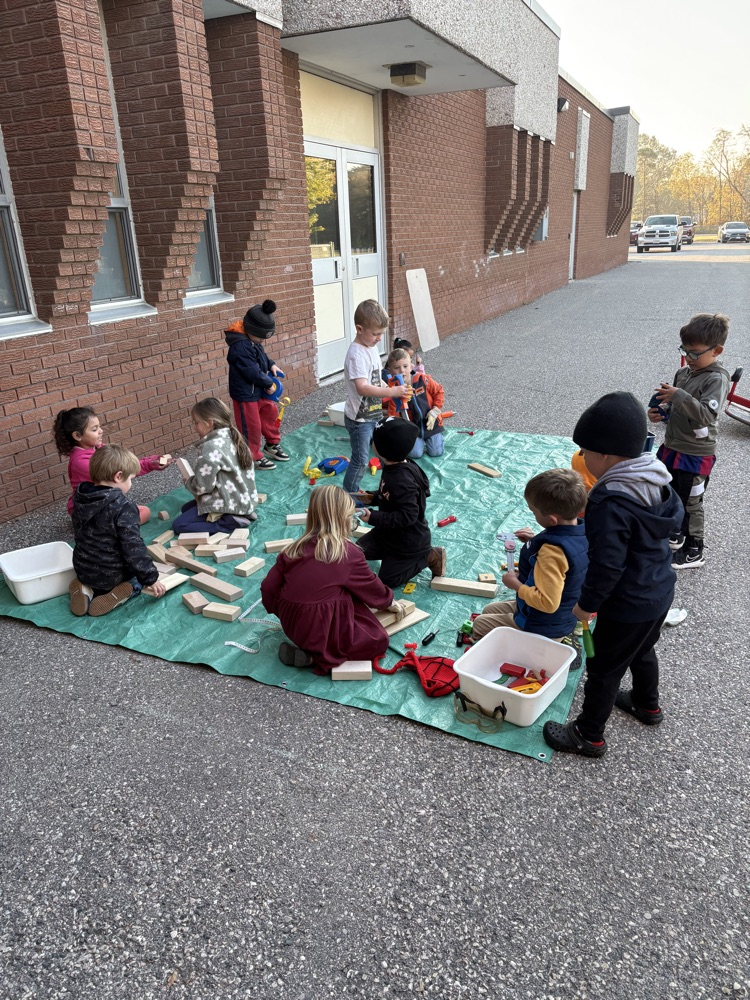 Kindergarten students sitting outside on a green tarp learning together
